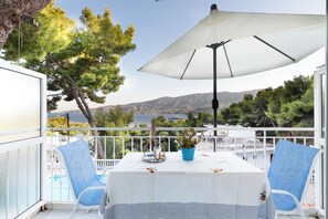 A balcony with a table set for two, overlooking a scenic view of a lake and mountains. - Lions Apartments  (Poros)