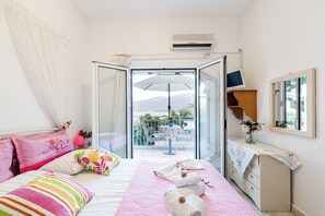 A hotel room with a bed, a dresser, a balcony with a table and chairs, and a view of the outdoors. - Lions Apartments  (Poros)