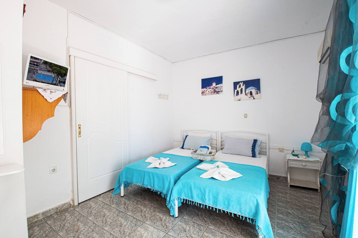 A room with two beds, a small bedside table, a wall-mounted TV, and a door.