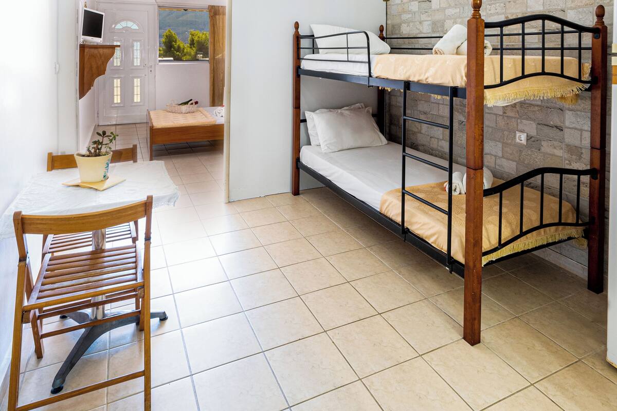 A room with a bunk bed, a wooden table with a chair, and a white door.