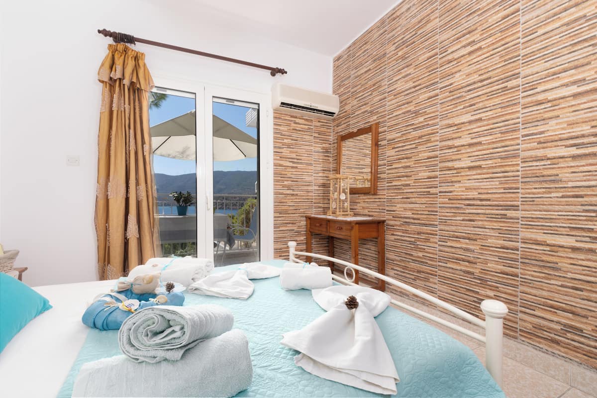 A hotel room with a bed, towels, a wooden wall, a window with curtains, and a view of the outdoors.