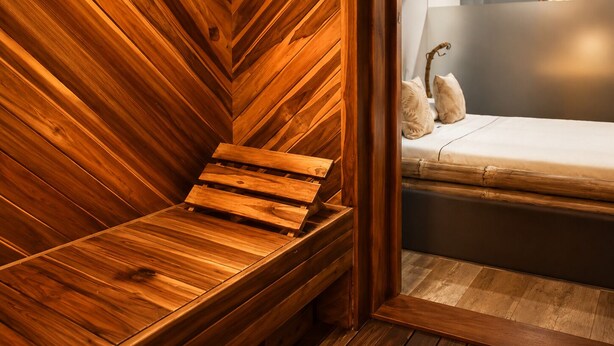 A wooden sauna bench with a slatted design, a bed with a white mattress and decorative pillows, and a wall-mounted mirror. - Hotel Zensual (Bogotá)
