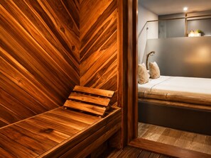 A wooden sauna bench with a slatted design, a bed with a white mattress and decorative pillows, and a wall-mounted mirror. - Hotel Zensual  (Bogotá)