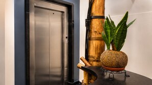 An elevator with a metallic finish, a bamboo pillar, and a potted plant with a woven base. - Hotel Zensual (Bogotá)
