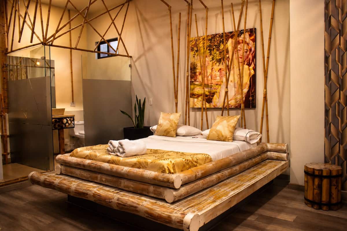 A room with a bed, a painting, and a bamboo structure.
