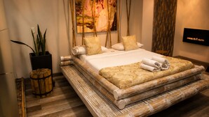 A bed with a wooden frame, a large painting on the wall, and a potted plant. - Hotel Zensual (Bogotá)