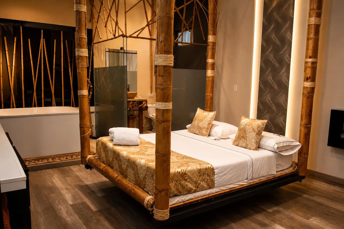 A four-poster bed with a canopy, a wooden floor, a white bedside table, and a bathroom with a modern design.
