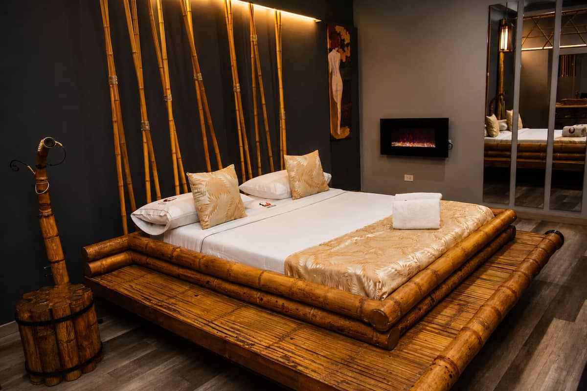 A bed with a bamboo frame, a television on the wall, and a wooden barrel.