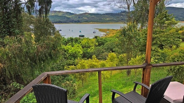Une terrasse en bois, dotée de chaises en osier, qui offre une vue sur un lac où naviguent des bateaux.