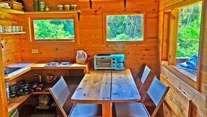 L’intérieur d’un chalet en bois comprend une table à manger, des chaises, une machine à café et deux fenêtres donnant sur la forêt.