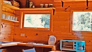 L’intérieur chaleureux de ce chalet est doté de murs en bois, d’un coin cuisine équipé d’un four à micro-ondes, d’une bouilloire et d’une machine à café, ainsi que de deux fenêtres offrant une vue sur la verdure.