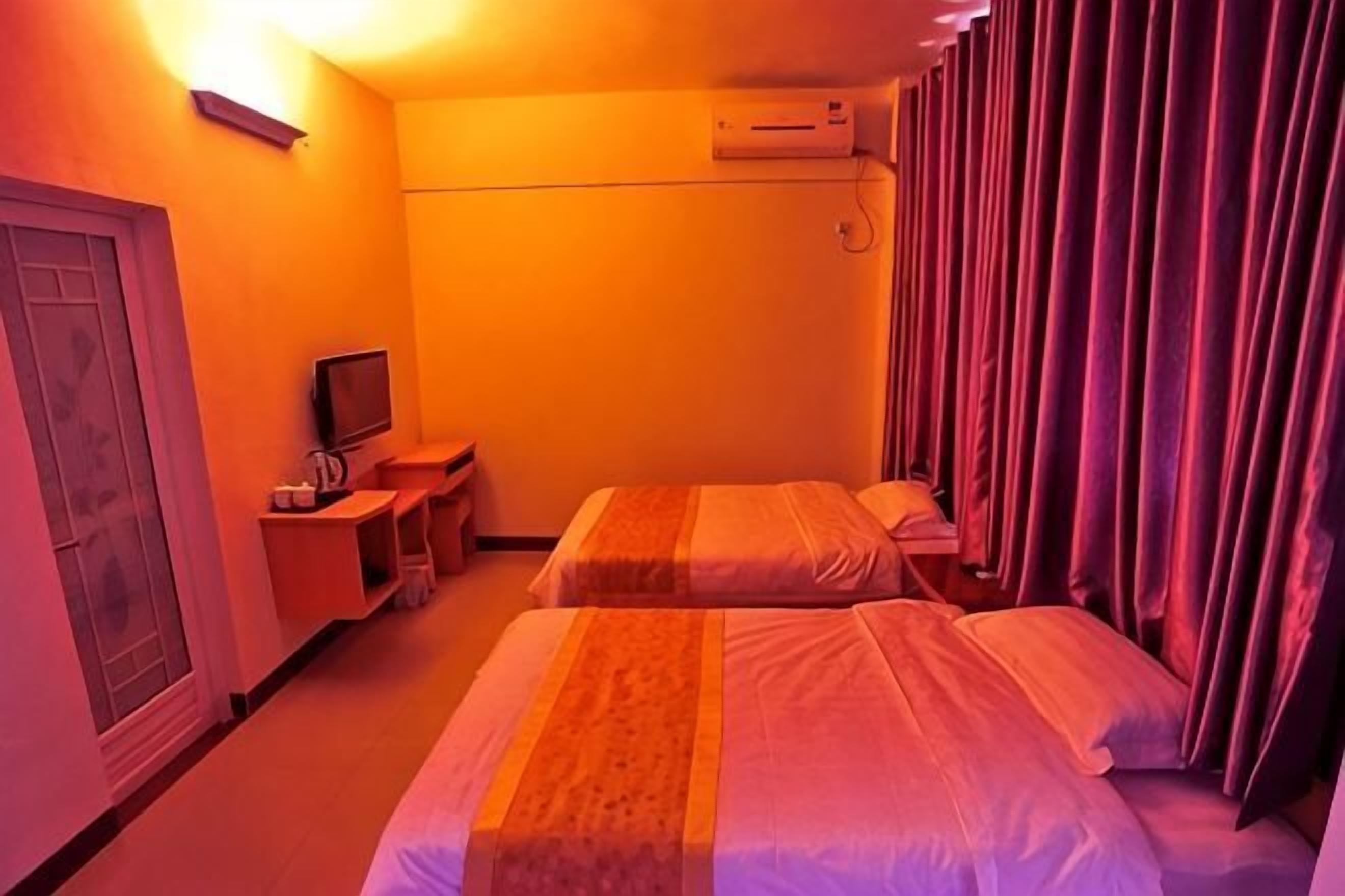 A hotel room with two beds, a TV, a desk, and an air conditioning unit.