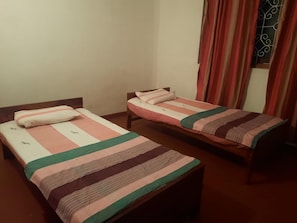Two single beds with wooden frames and striped bedding in a room with plain walls and a window with curtains.