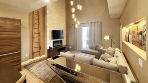 Ein modernes Wohnzimmer mit einer großen Eckcouch, einem Flachbildfernseher und einer Treppe, die in ein Obergeschoss führt.