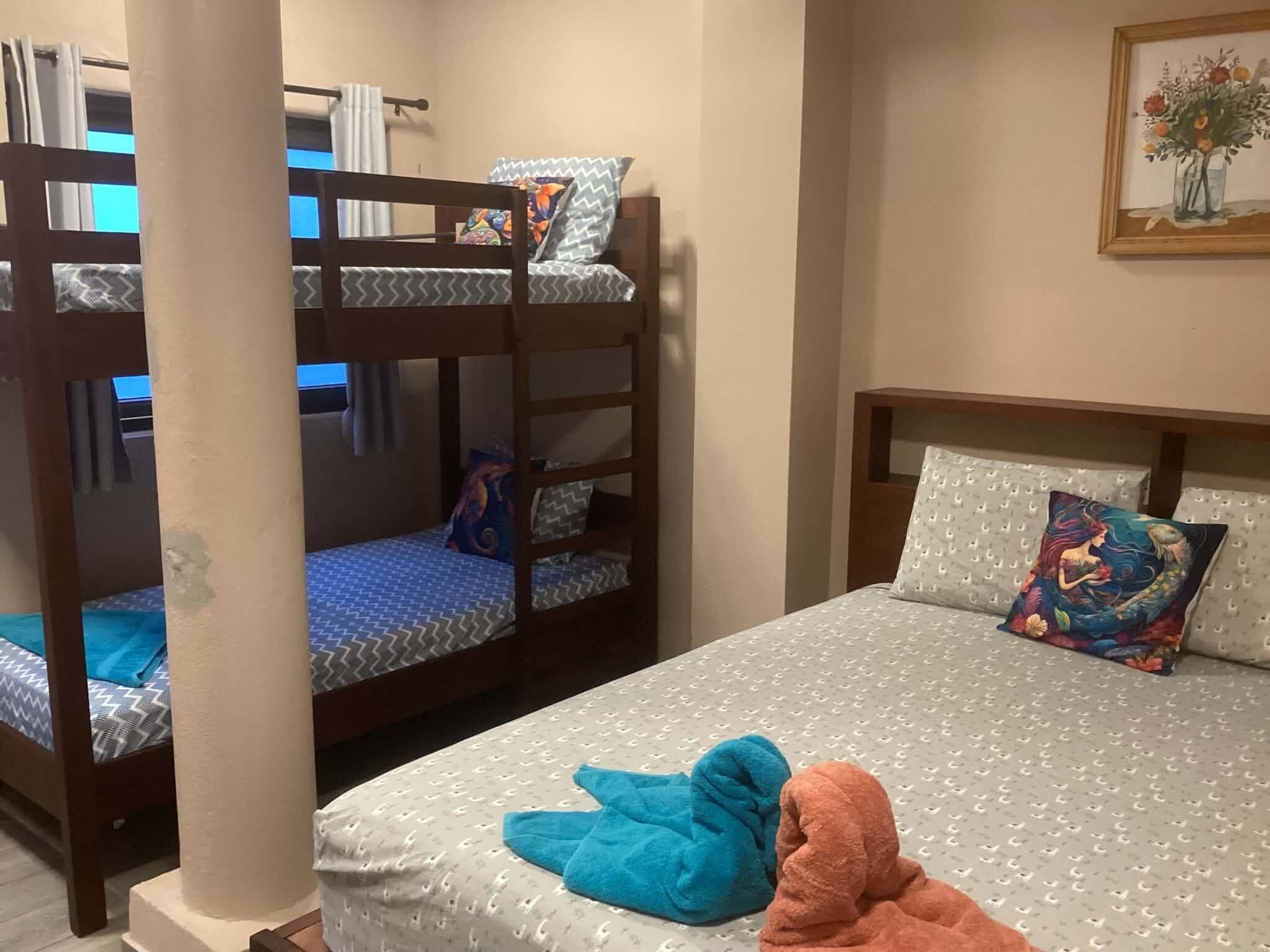 Een stapelbed met beddengoed en kussens met een patroon, een enkel bed met een beddeken met een patroon en decoratieve kussens, en een schilderij aan de muur.
