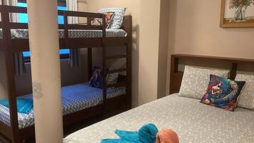 Een stapelbed met beddengoed en kussens met een patroon, een enkel bed met een beddeken met een patroon en decoratieve kussens, en een schilderij aan de muur.