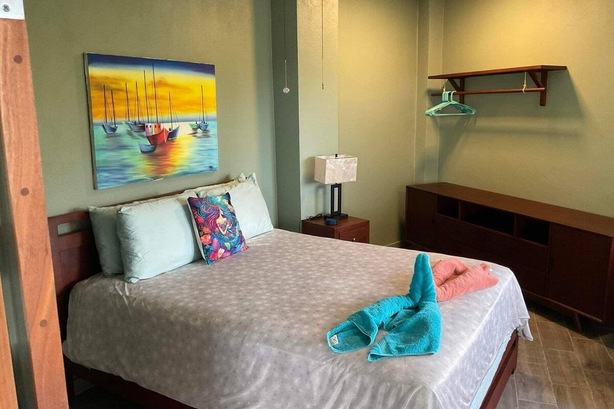 A neatly made bed with a patterned bedspread, a colorful pillow, and a folded towel on the bed.