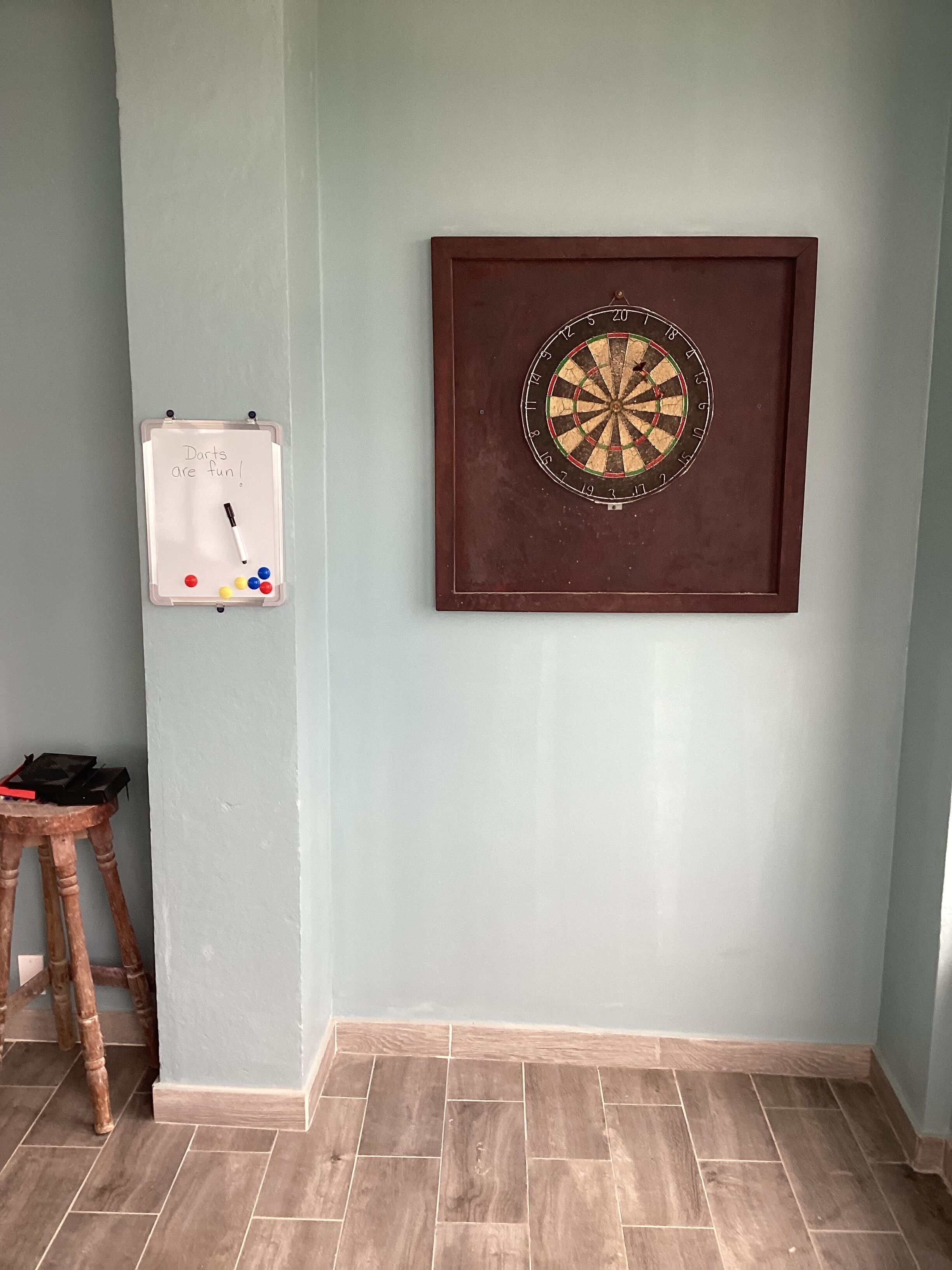 A dartboard mounted on a wall, a whiteboard with writing, and a wooden stool.