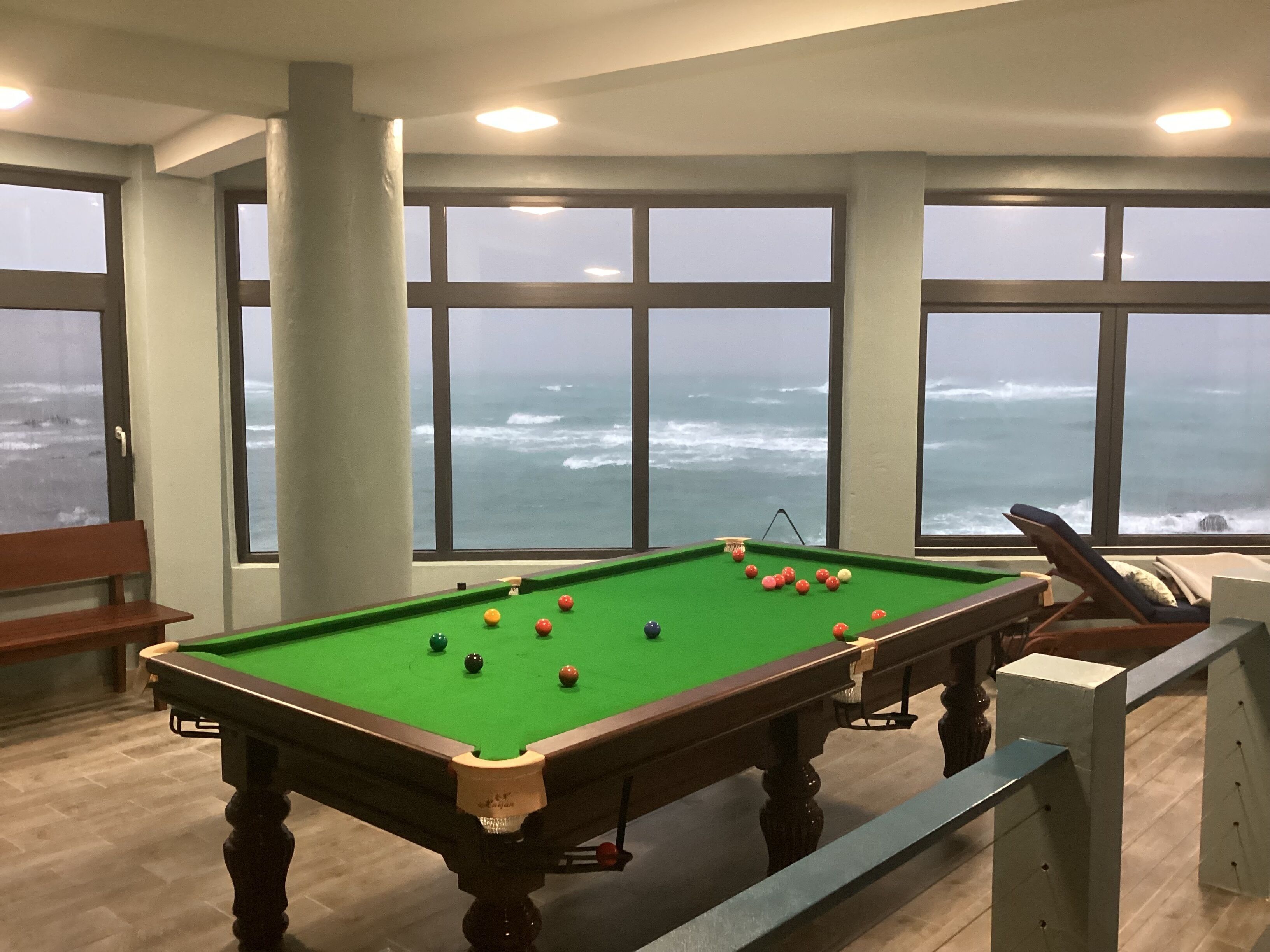 A pool table with balls in a room with large windows overlooking the ocean.