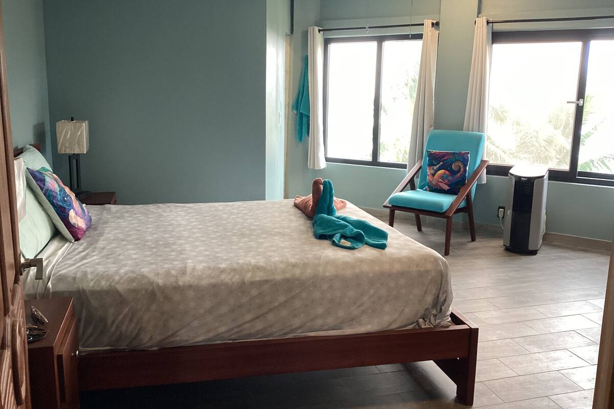 A hotel room with a bed, a chair, a lamp, and a window.