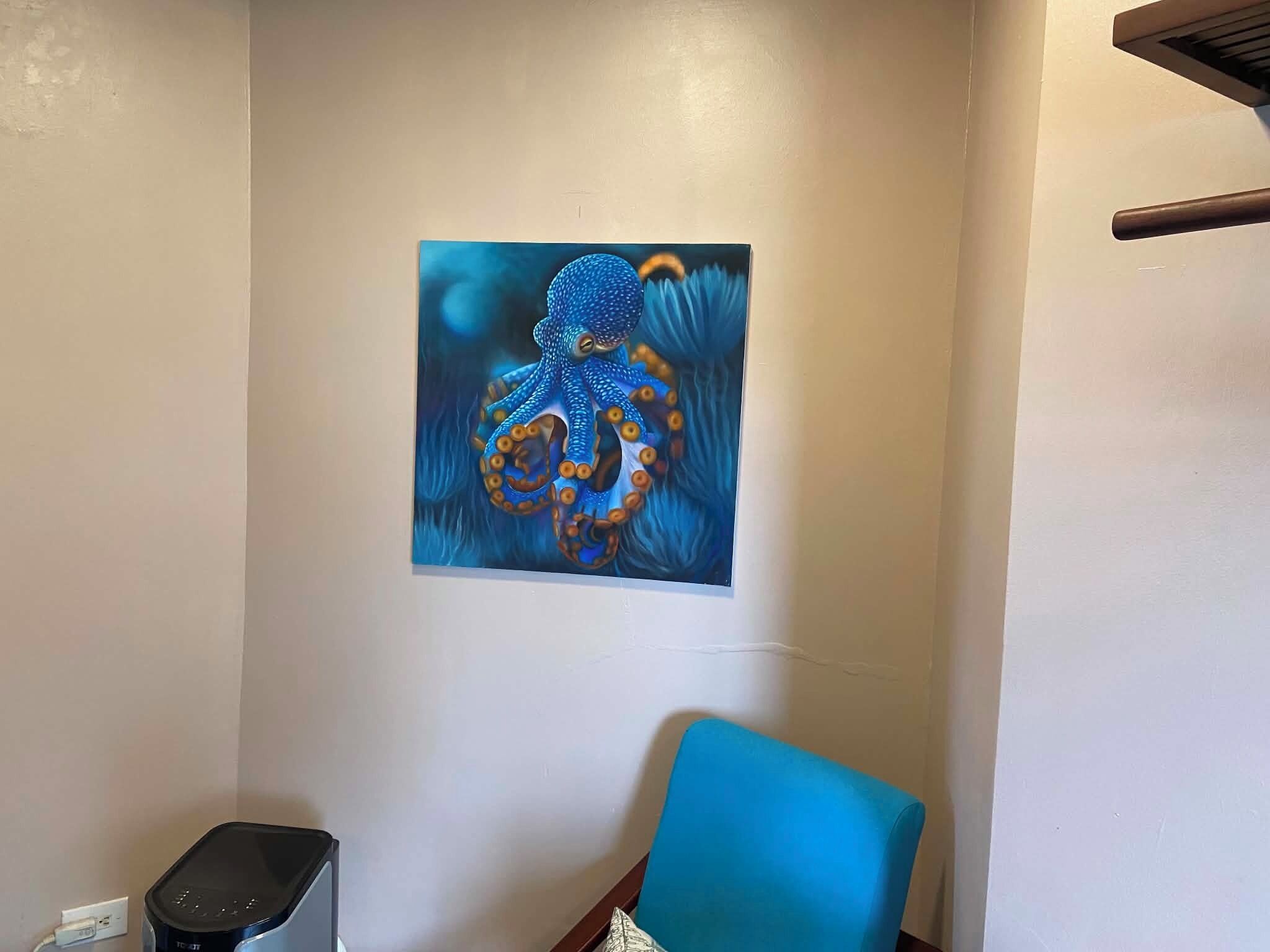 A room with a painting of an octopus on the wall, a blue chair, and a small table.