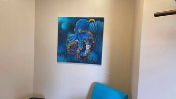 A room with a painting of an octopus on the wall, a blue chair, and a small table.