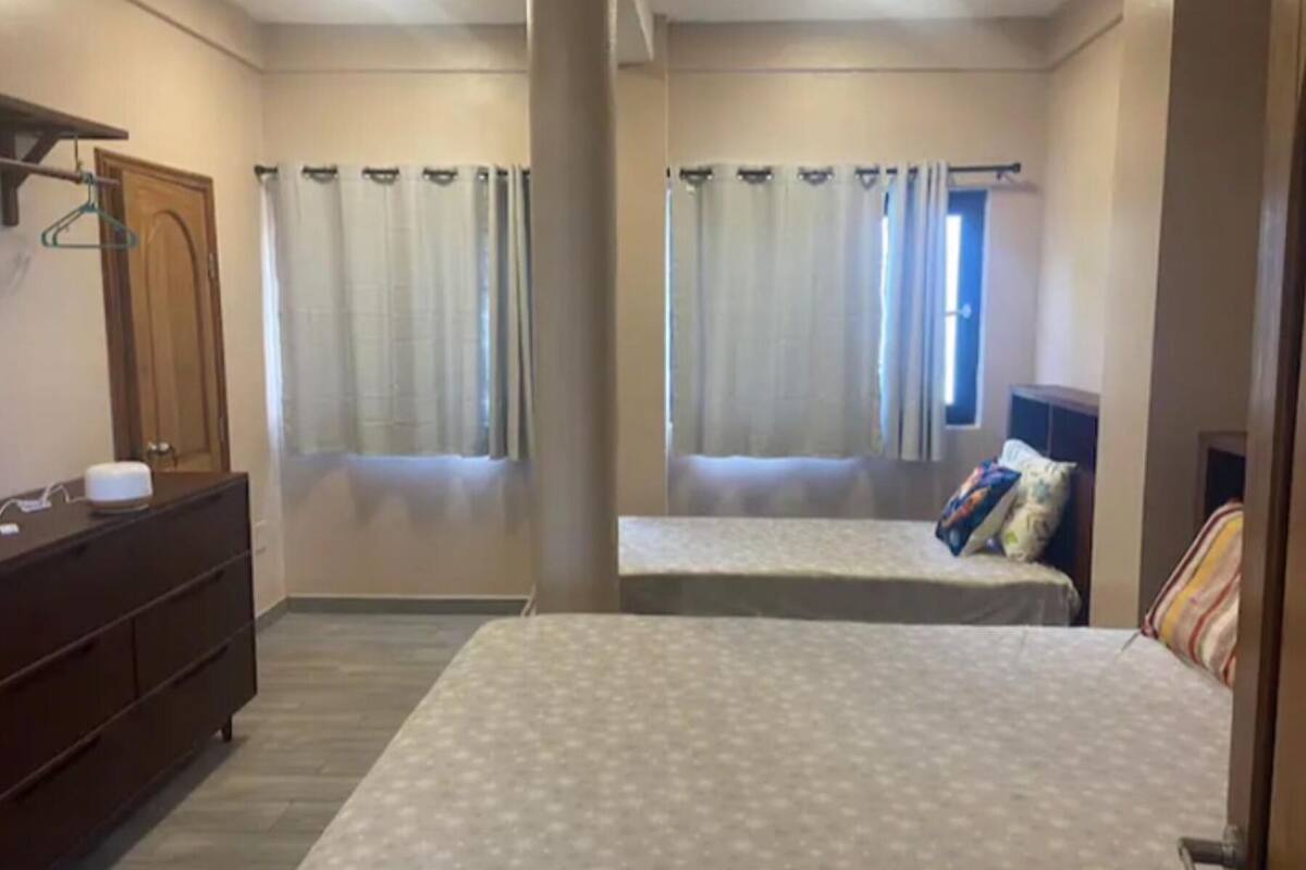 A bedroom with two beds, a dresser, and a window with curtains.