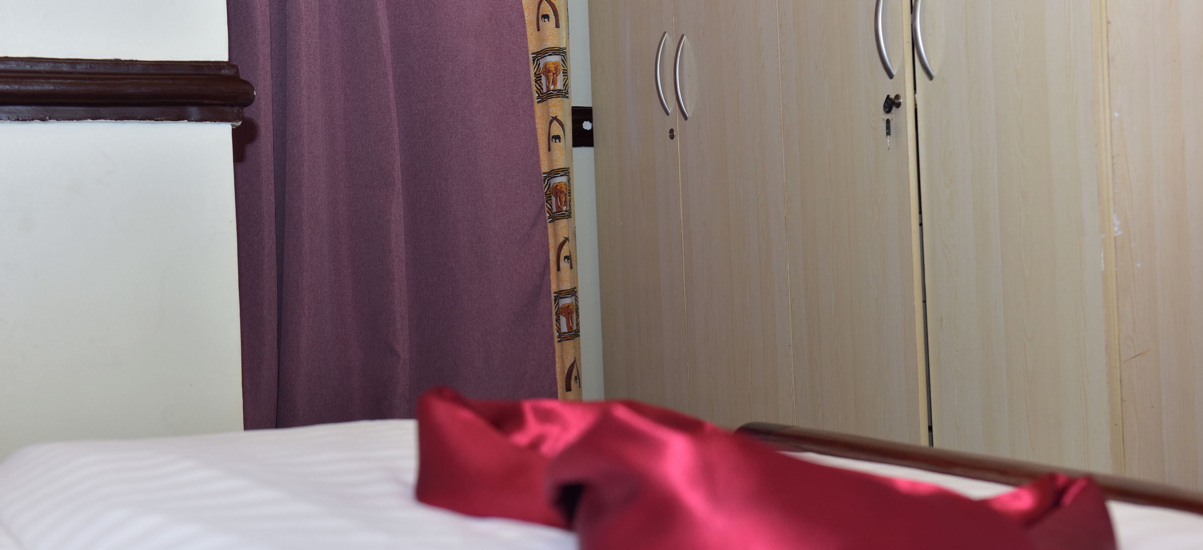 A bed with a white sheet, a purple curtain, and a wooden headboard.