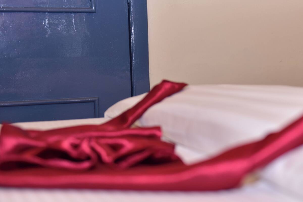 A bed with white sheets and a red garment on it.
