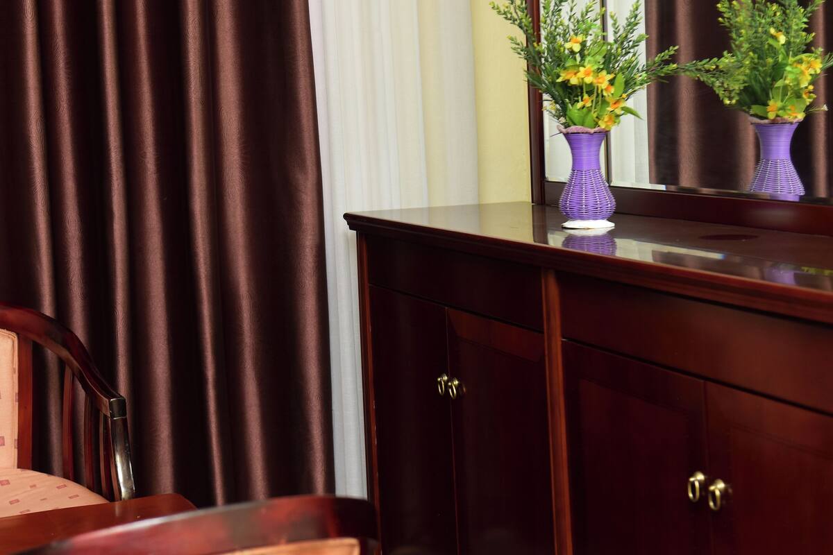 A room with a wooden chair, a dark brown cabinet, and a mirror reflecting a vase with flowers.