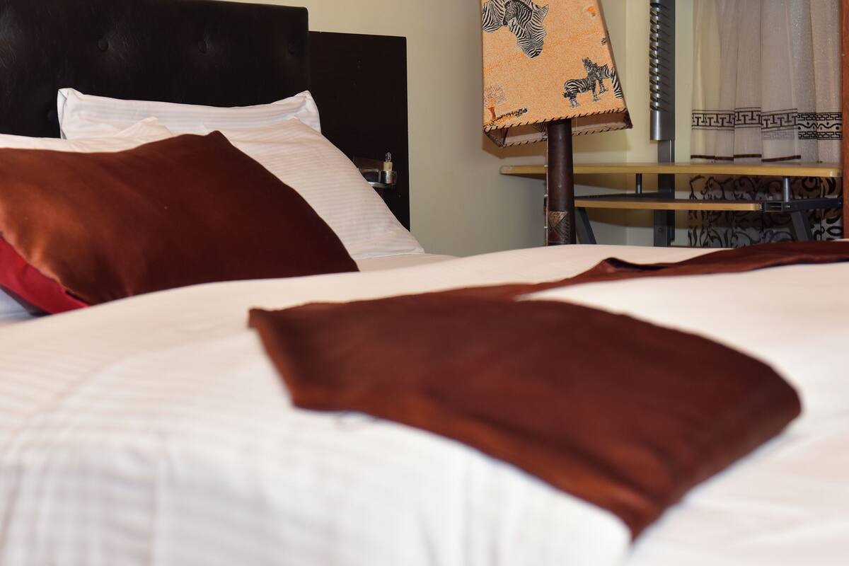 A neatly made bed with white and brown bedding, a dark headboard, and a bedside table with a lamp.