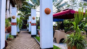 A pathway leading to a covered seating area with a red canopy, surrounded by potted plants and a brick structure. - New Zebra Hotel (Kigali)