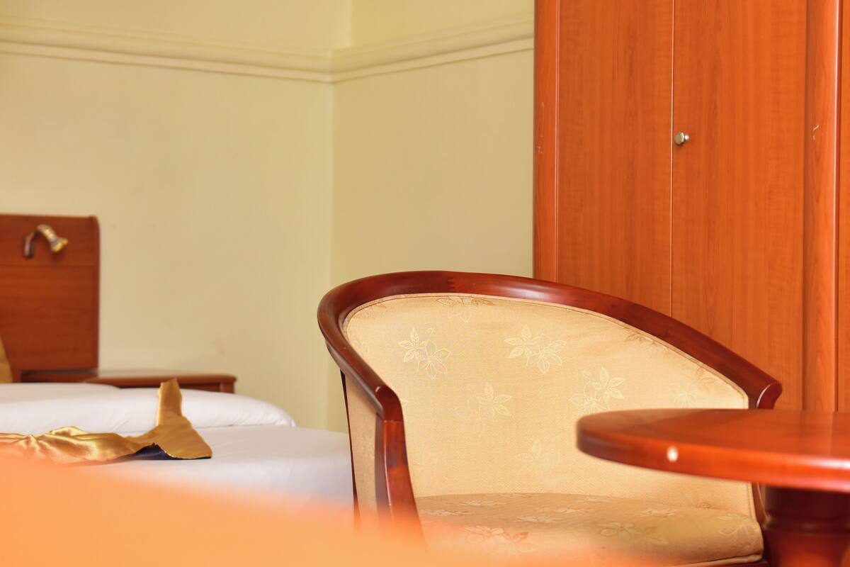 A hotel room with a bed, a wooden nightstand, a chair, and a small table.