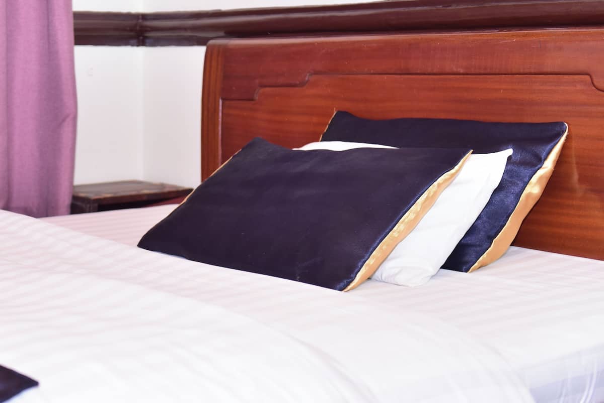 A neatly made bed with a dark blue pillow and a white pillow, a black throw blanket, and a wooden headboard.