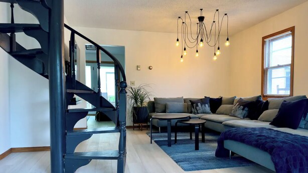 Una sala de estar moderna con una escalera espiral, un conjunto de sofás, una mesa de centro y una araña.
