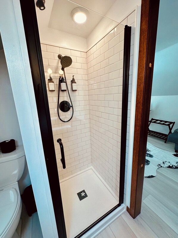 Une salle de bain moderne avec des carreaux de céramique blancs rectangulaires, une douche en verre, des toilettes et un lavabo.