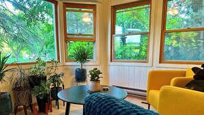 Una habitación con una mesa redonda, un sofá amarillo y varias macetas con plantas.