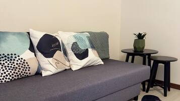 Una sala de estar moderna con un sofá gris, cojines estampados, una mesita redonda con una planta y una alfombra original.