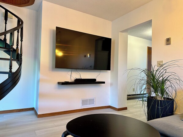 Una sala de estar moderna con un televisor de pantalla plana montado en la pared, una escalera de madera y una planta en maceta.