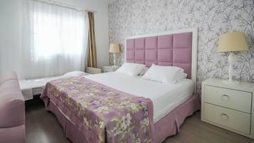 Una camera d'albergo con un letto, un comodino, una lampada, una sedia e una finestra con tende.