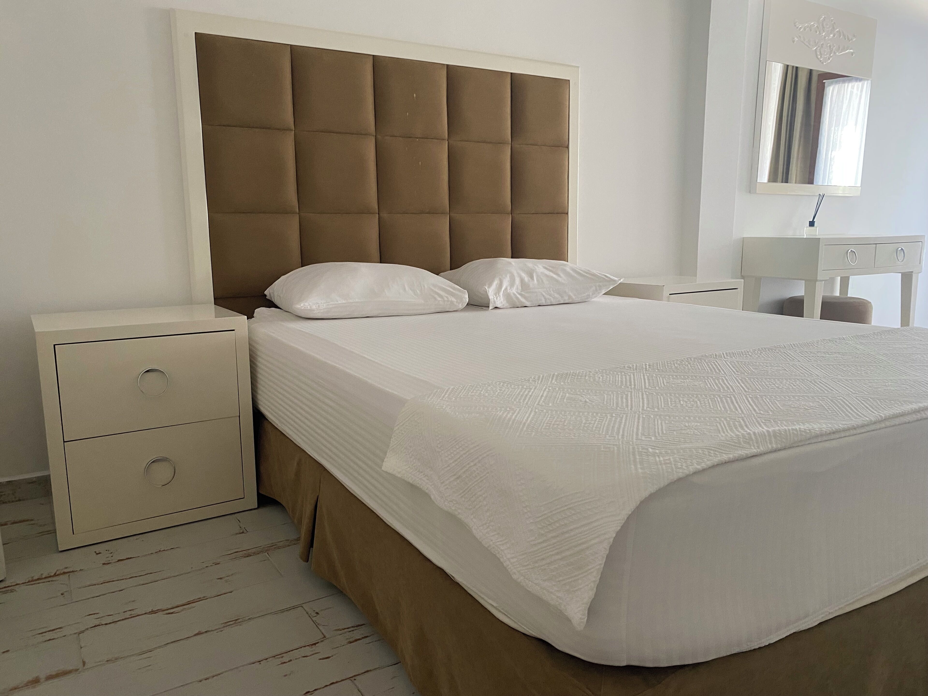 A bedroom with a large bed, a nightstand, a dresser, and a mirror.