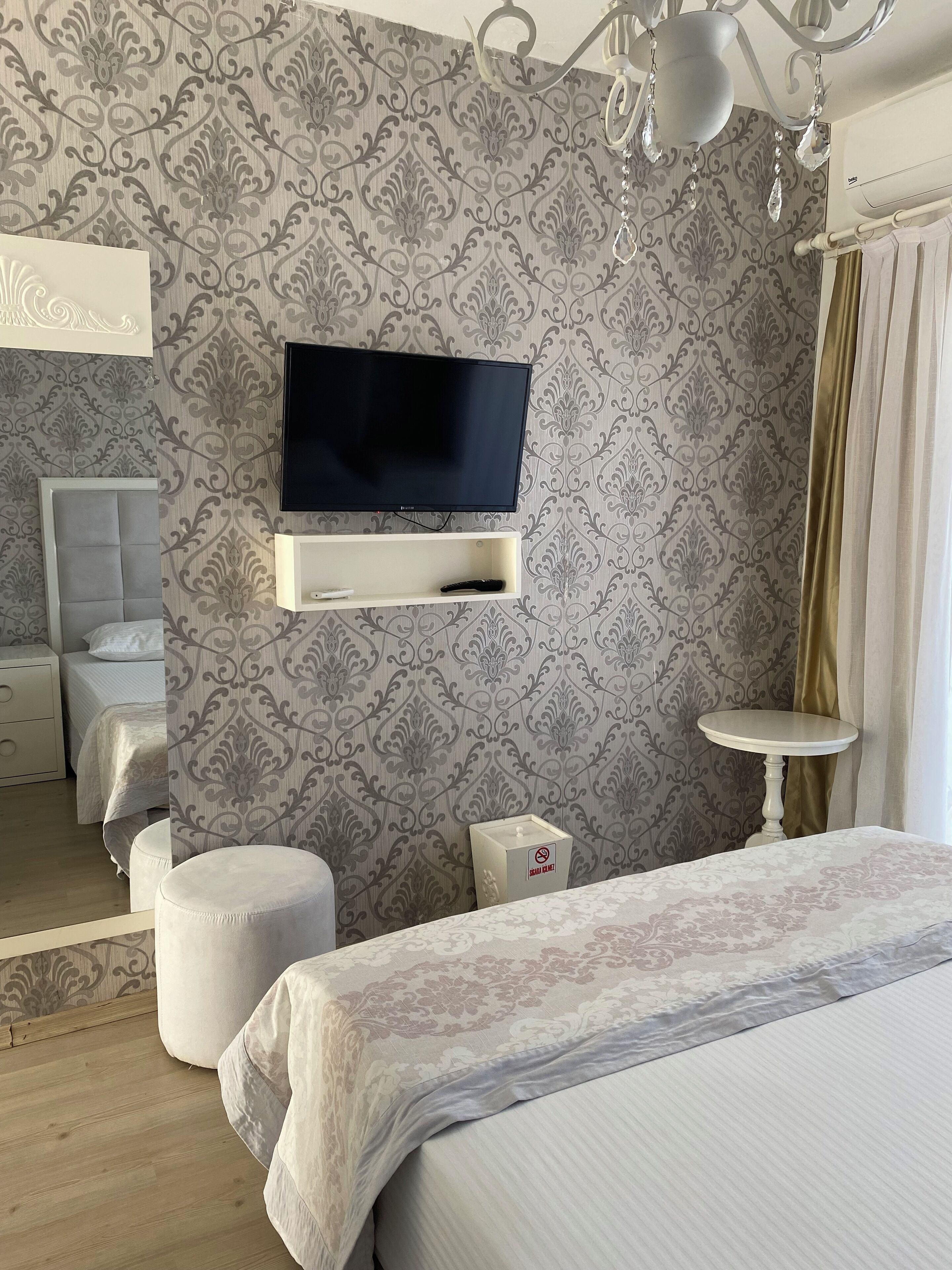 A bedroom with a TV mounted on the wall, a bedside table, a bed with a patterned bedspread, and a nightstand with a lamp.