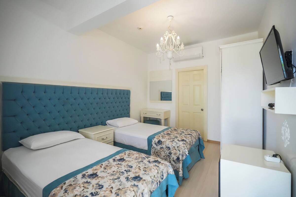 A hotel room with two beds, a TV, a desk, and a chandelier.