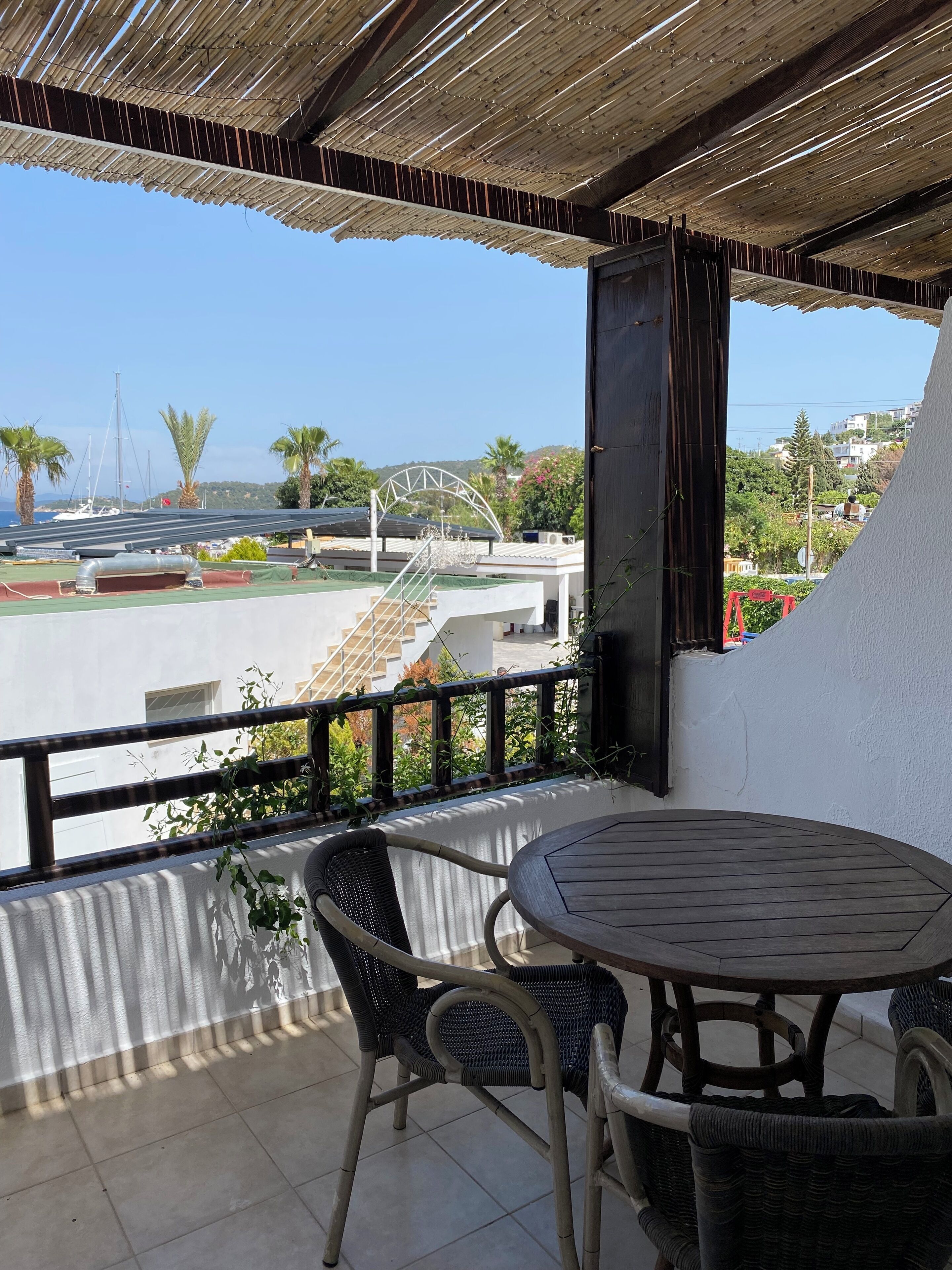 Un balcón con una mesa y sillas, con vista a un puerto deportivo con barcos y un puente.
