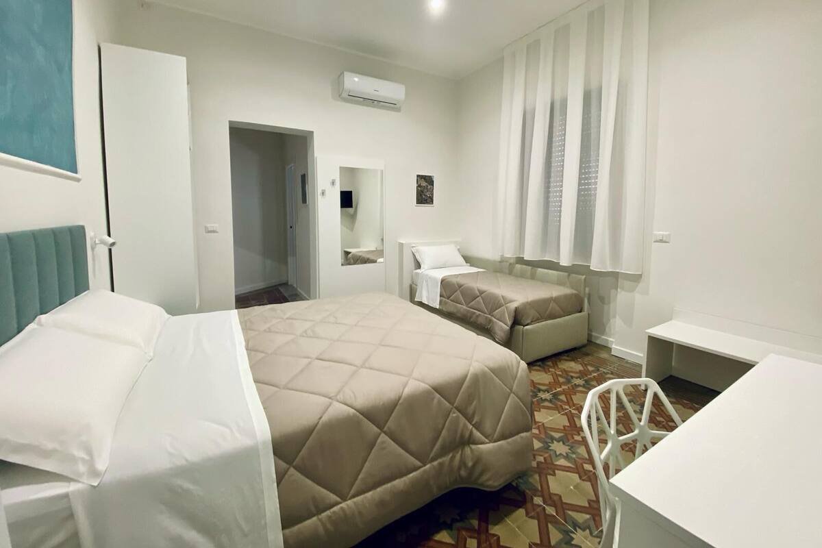 A hotel room with two beds, a desk, a chair, a mirror, and a window with curtains.