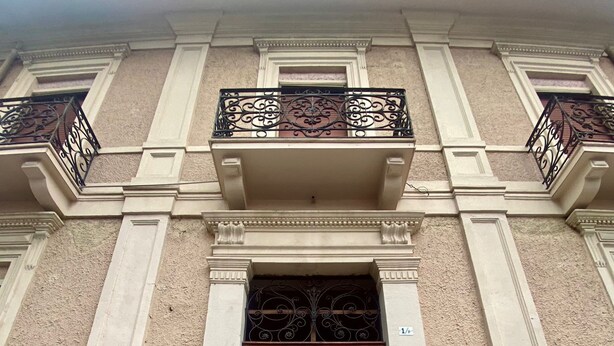 En byggnadsfasad med en stor, dubbel trädörr, utsmyckade metallräcken på balkongen och flera skyltar, inklusive "R&B Helioc" och "SEDE PROVINCIAL".