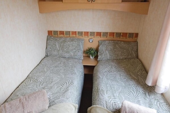 A compact RV interior with two beds, a small table, and a potted plant. - Comfortable Mobile Home in the Countryside (Birra)