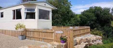 A mobile home with a fenced yard, a small garden, and a sign indicating 'B&B Way'.
