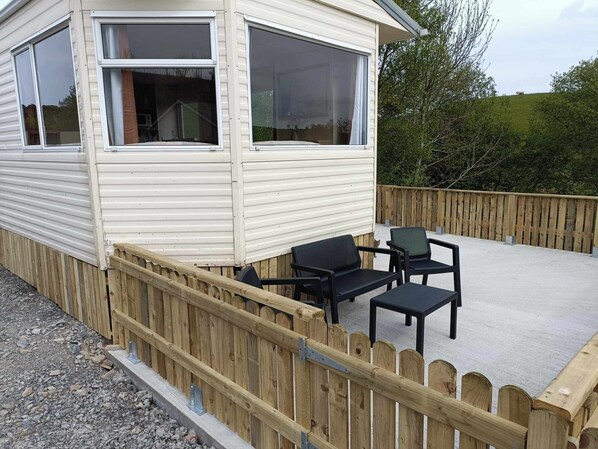A wooden deck with outdoor furniture, a wooden fence, and a building with large windows. - Comfortable Mobile Home in the Countryside (Birra)