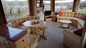A cozy interior with a sofa, a small table, a TV, and a view of the outdoors. - Comfortable Mobile Home in the Countryside (Birra)